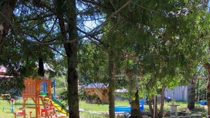 Un parque infantil con un tobogán y estructuras para escalar, rodeado de árboles y troncos de madera dispuestos en círculo.