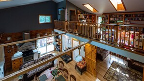 Un loft espacioso con techo alto, vigas de madera, un entrepiso y una amplia colección de libros.
