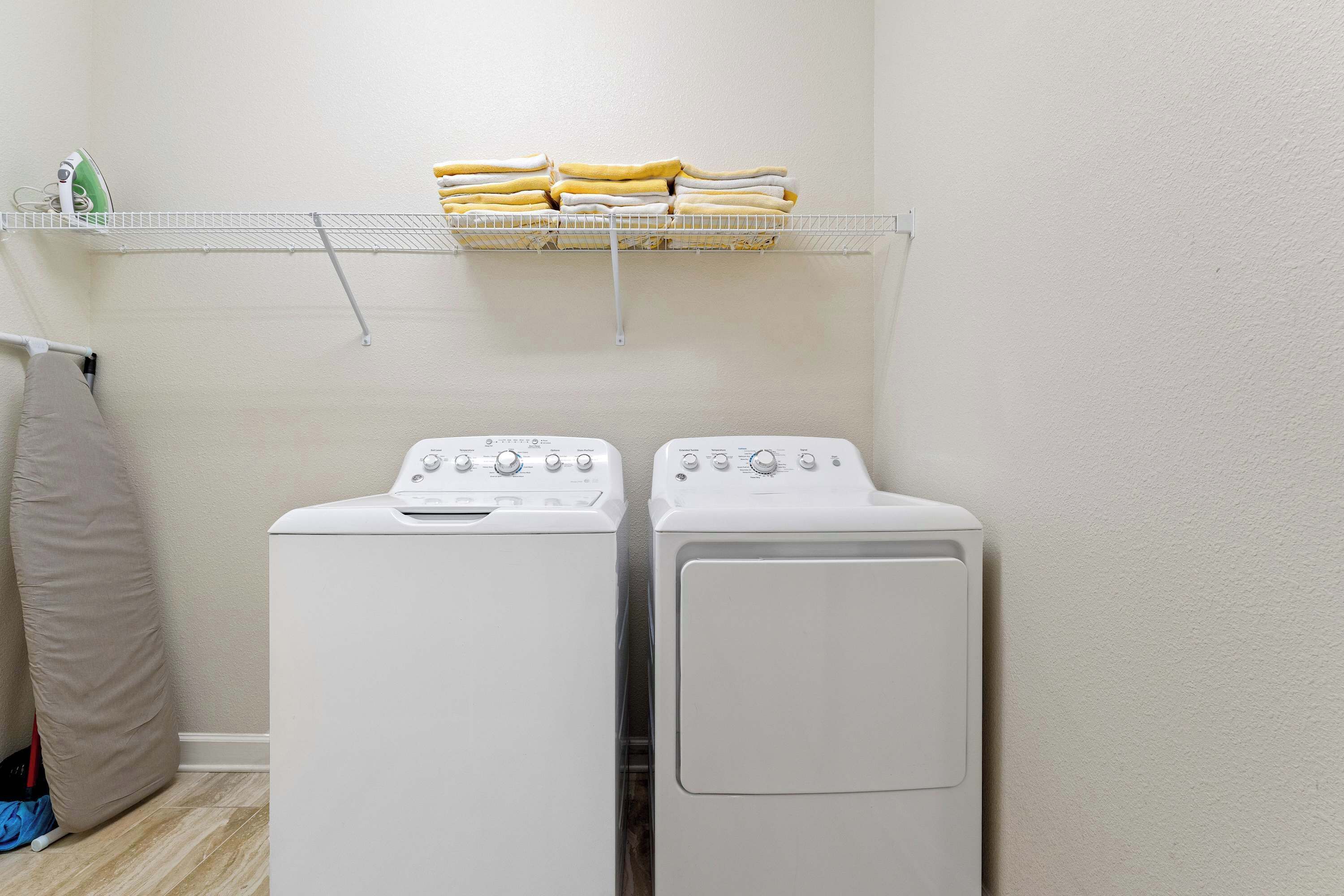 A laundry area with two front-loading washing machines and a shelf above holding folded towels.