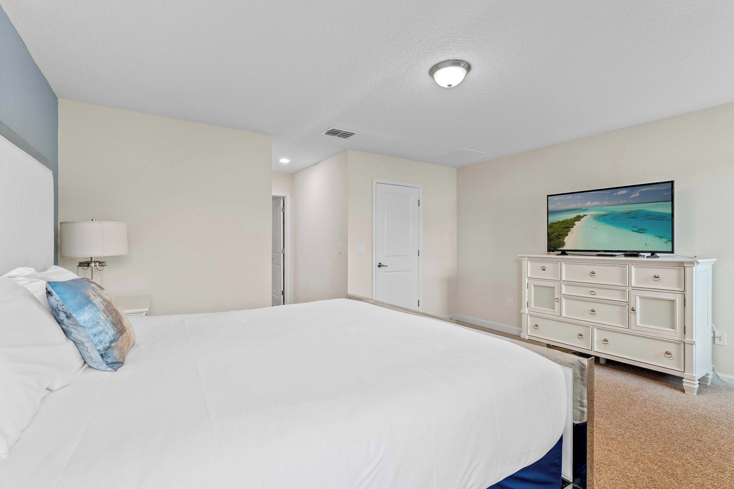 Een hotelkamer met een groot bed, een televisie op een dressoir, en een deur naar een andere kamer.