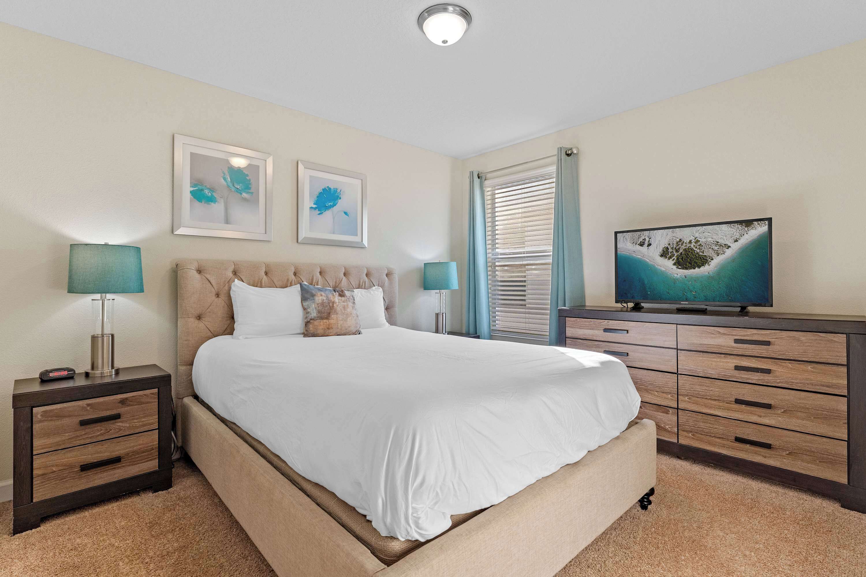 A bedroom with a bed, nightstands, a dresser, and a television.
