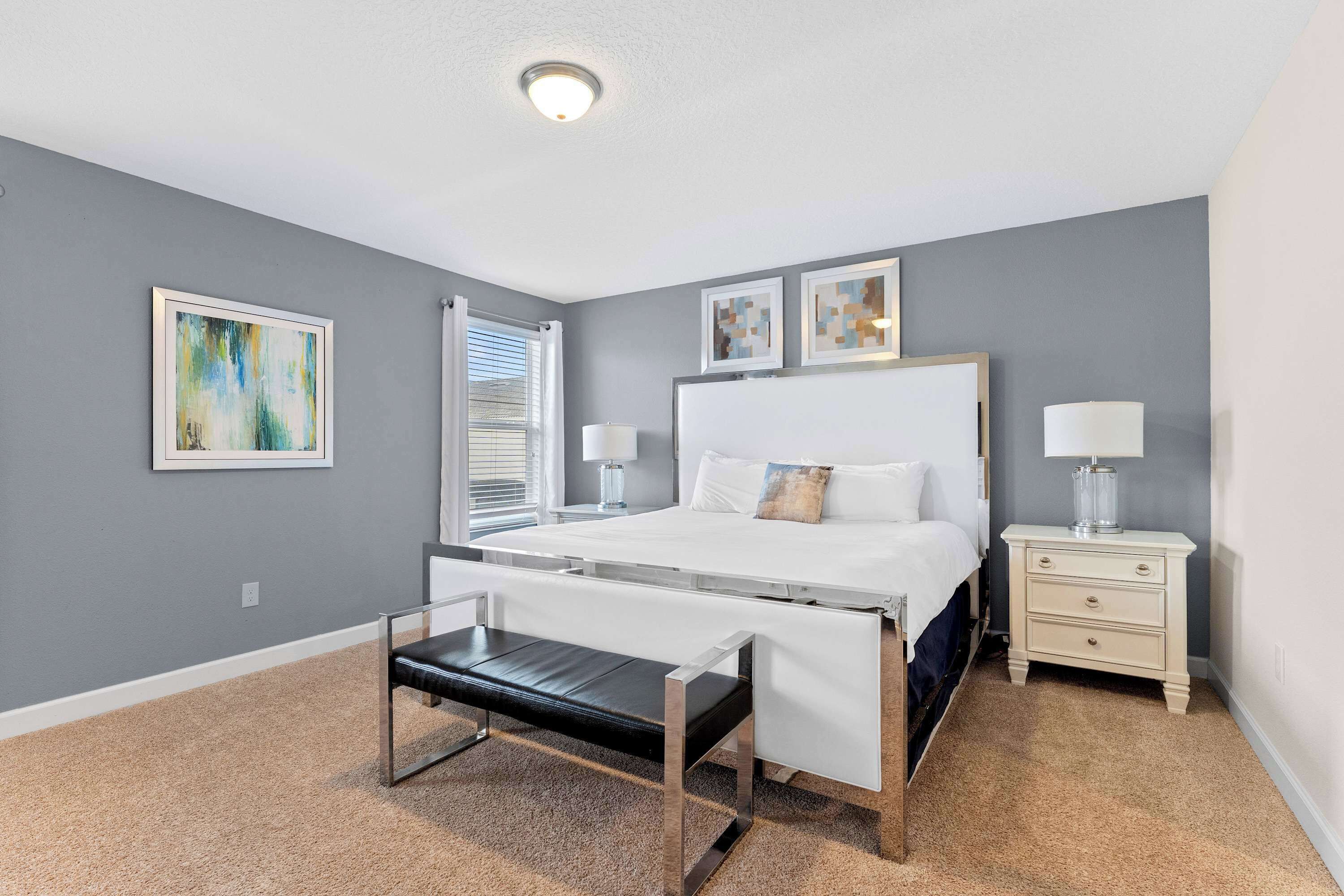 A bedroom with a bed, bedside tables, a bench, and artwork on the walls.