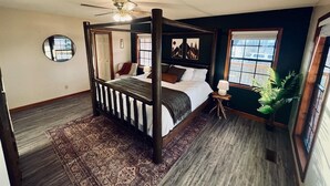 A bedroom with a four-poster bed, a ceiling fan, a large window with blinds, and a decorative mirror on the wall. - Spacious Home •Pet Friendly •Mtn Views & Firepit! (Sevierville)
