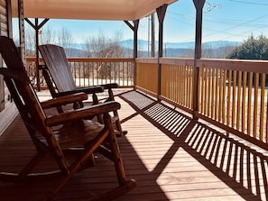 A wooden deck with two rocking chairs and a covered area, overlooking a mountainous landscape. - Spacious Home •Pet Friendly •Mtn Views & Firepit! (Sevierville)