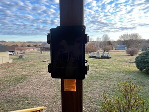 A black electrical box mounted on a wooden post with a grassy yard and a distant view of houses.