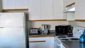 Une cuisine de taille réduite, avec des meubles blancs, un réfrigérateur, une cuisinière, un four à micro-ondes et un grille-pain.