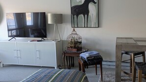 Une chambre à coucher comprenant un lit, un téléviseur, un bureau avec une lampe, une chaise, une cage à oiseaux et un tableau représentant des chevaux.