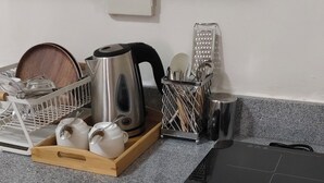 Una encimera de cocina con cafetera, hervidor y utensilios. Debajo, hay un lavavajillas y un refrigerador.