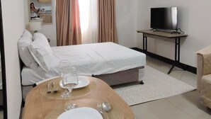 Habitación de hotel con cama, televisión, mesa de comedor con cubiertos y un espejo que refleja la habitación.