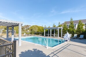 A swimming pool with lounge chairs and a pergola, surrounded by a fence and trees.