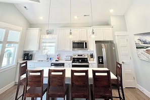 A modern kitchen with white cabinets, a central island, and a dining area with wooden chairs.
