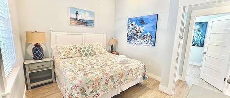 Ein Schlafzimmer mit einem Bett, einem Nachttisch, einer Lampe, einem Deckenventilator und zwei an der Wand hängenden Bildern.