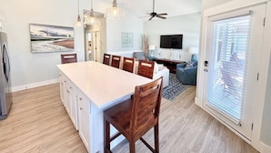 A modern kitchen with a large island, dining chairs, pendant lights, and a ceiling fan.