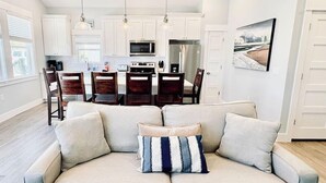 A modern living room with a grey sofa, a patterned throw pillow, and a dining area with wooden chairs and a table.