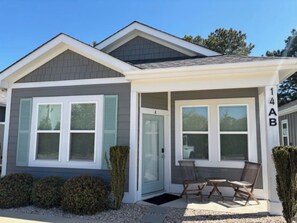 Ein zweistöckiges Haus mit einer Veranda, einer Tür und einer kleinen Sitzgelegenheit im Freien.