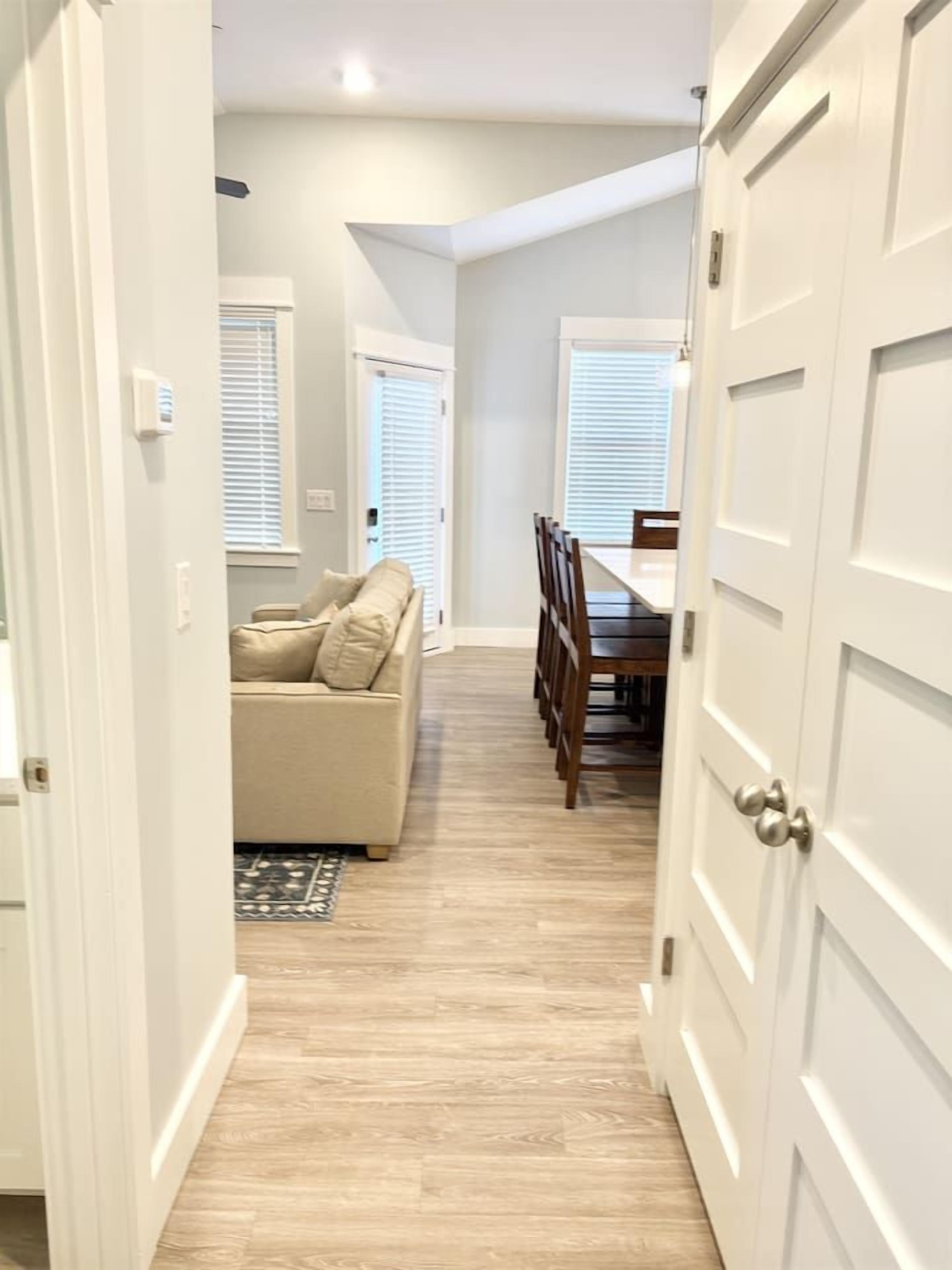 A hallway with a beige sofa, dining table, and chairs, leading to a room with a door.
