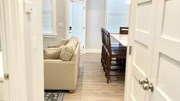A hallway with a beige sofa, dining table, and chairs, leading to a room with a door.