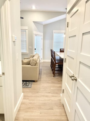 A hallway with a beige sofa, dining table, and chairs, leading to a room with a door.