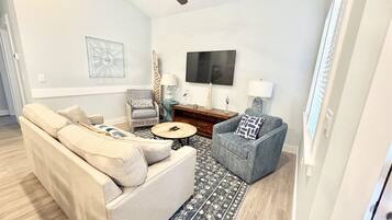 A living room with a sofa, armchair, coffee table, and a TV on the wall.