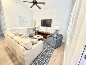 Ein Wohnzimmer mit Sofa, Sessel, Couchtisch und Fernseher an der Wand.