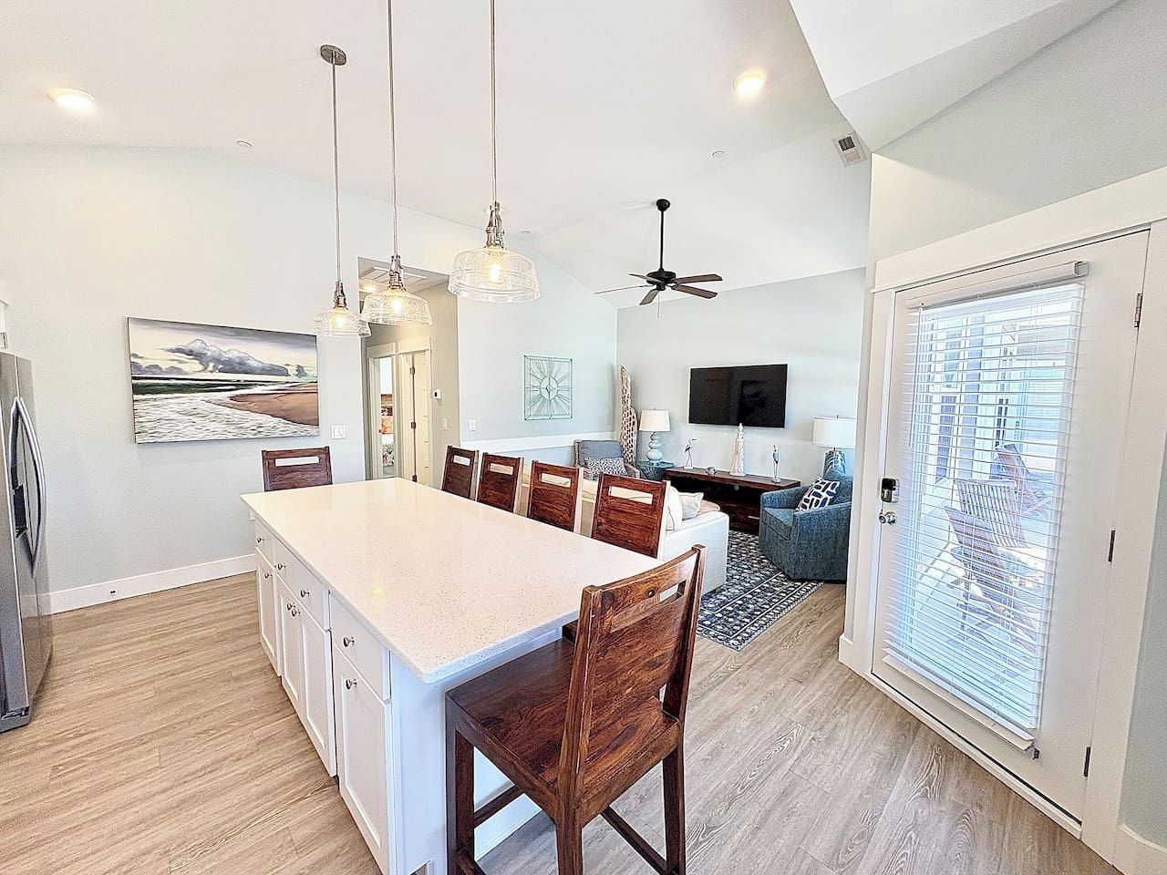 A modern kitchen with a large island, dining chairs, pendant lights, and a ceiling fan.