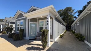 A modern residential building with a covered porch, a small garden, and a clear sky.