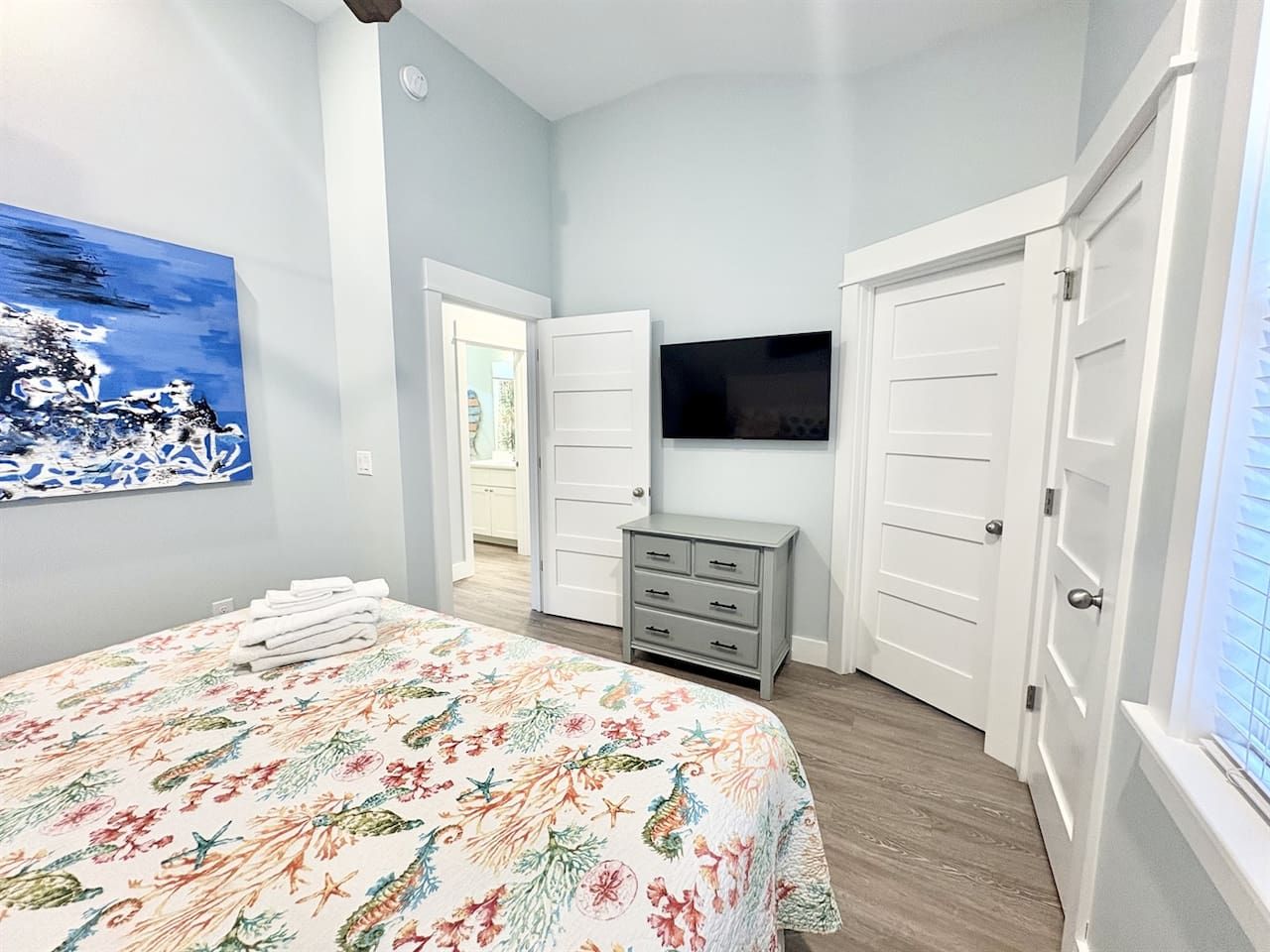 A bedroom with a bed, a dresser, a television, and a door leading to another room.