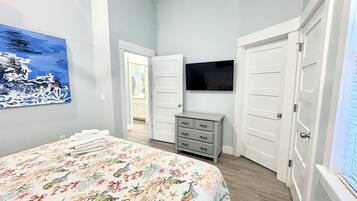 A bedroom with a bed, a dresser, a television, and a door leading to another room.