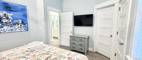 Een slaapkamer met een bed, een dressoir, een televisie en een deur die naar een andere kamer leidt.