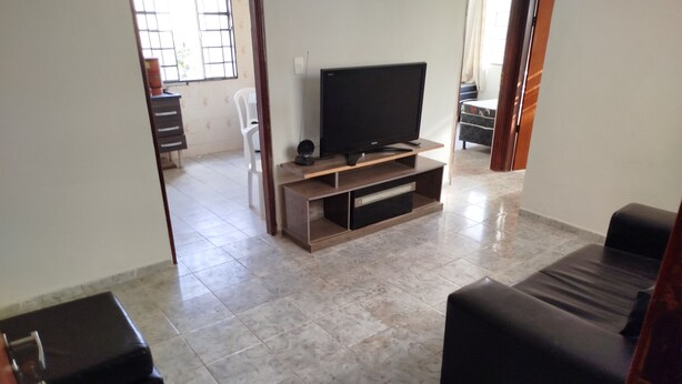 Una sala de estar con un televisor de pantalla plana sobre un soporte de madera, un sofá negro y un pequeño otoman negro.