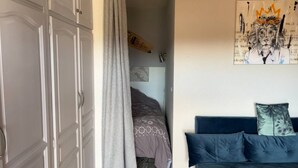 A bedroom with a bed, a blue sofa, a grey curtain, and a wall with a framed picture.