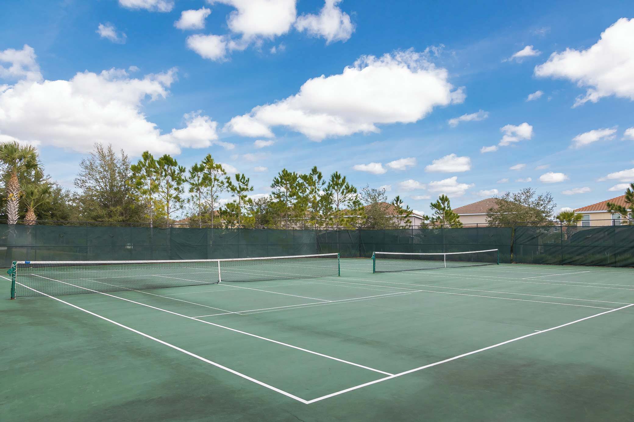 An outdoor tennis court with a net, surrounded by trees and a clear sky.