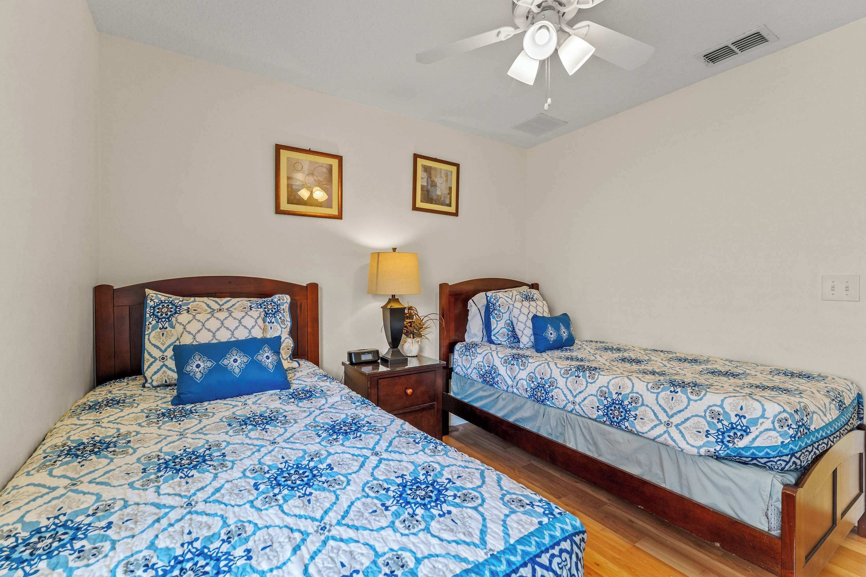 A bedroom with two beds, wooden headboards, a ceiling fan, and two wall-mounted lamps.