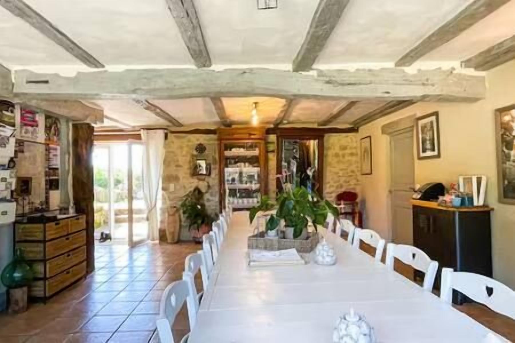 A long dining table with chairs, a kitchen area with cabinets, and a stone wall.