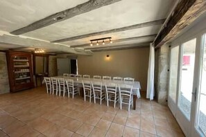 Una habitación amplia con una larga mesa de comedor y sillas, un armario de madera y un ventanal grande.