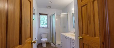 A narrow bathroom with wooden doors, a toilet, a shower enclosure, and a vanity with drawers.