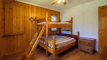 Un lit superposé en bois avec une échelle, une petite commode en bois et un ventilateur de plafond dans une pièce aux murs en bois.