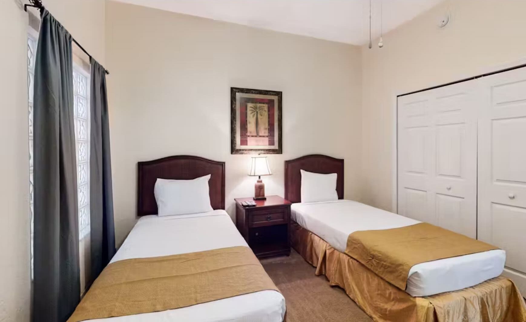 A hotel room with two single beds, a nightstand with a lamp, a framed picture on the wall, and a wardrobe.