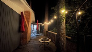 Un terrazzo in legno con tavolo e sedie, un muro in mattoni e luci a stringa.