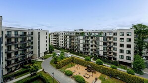 A modern apartment complex with multiple balconies, a central courtyard with a playground, and a well-maintained green space.