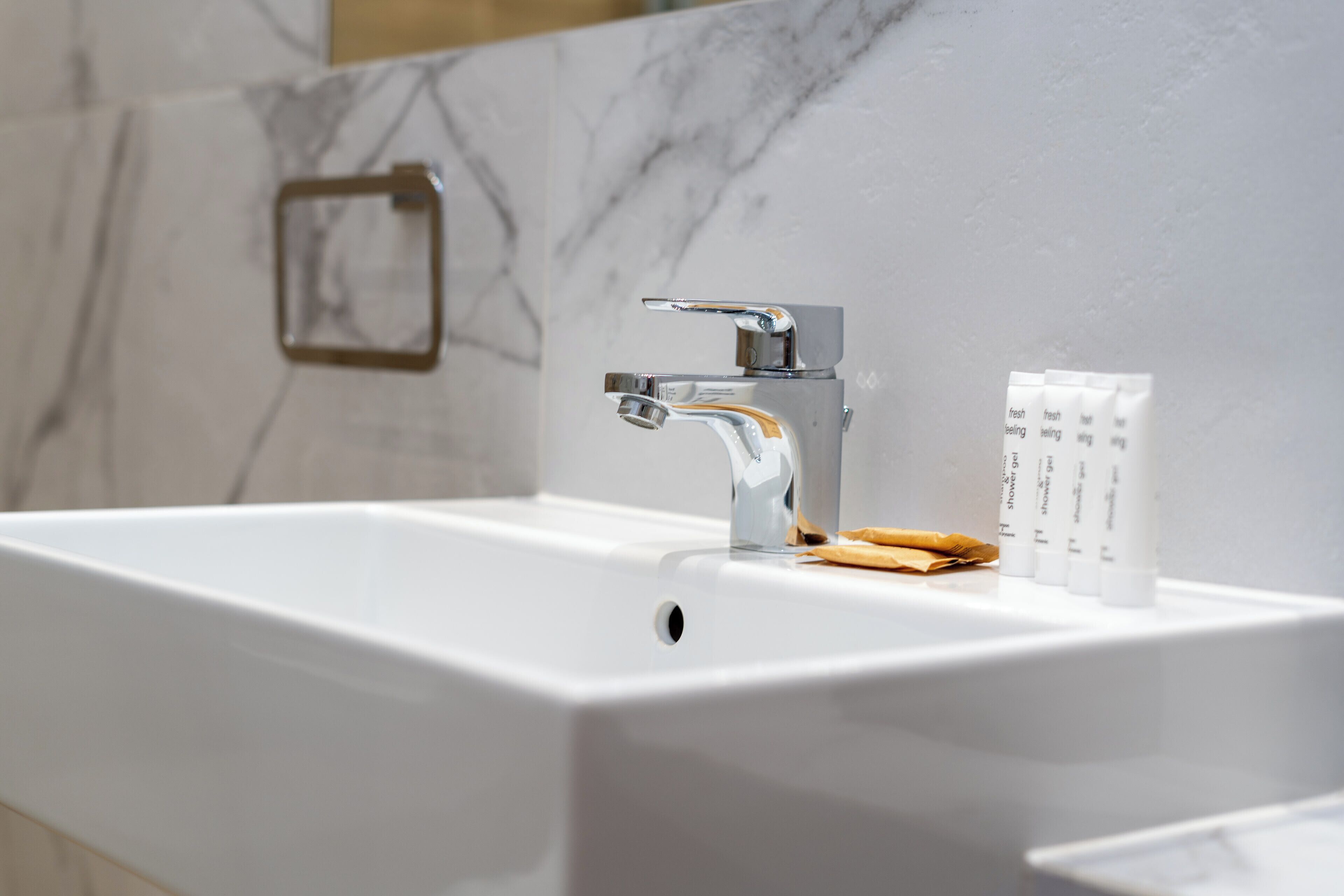 Ein modernes Badezimmer mit einem weißen Waschbecken, einem chromfarbenen Wasserhahn und einem Satz Pflegeprodukten.