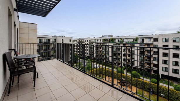 A balcony with a table and chairs, overlooking a residential area with modern buildings.