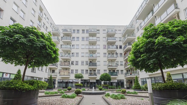 A modern apartment building with a central courtyard, featuring potted trees and a paved walkway. - Warta River Cozy Vibe Studio (Poznań)
