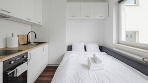 A modern, compact room with a kitchenette, a bed with white linens, and a window providing a view of the outside. - Warta River Cozy Vibe Studio (Poznań)