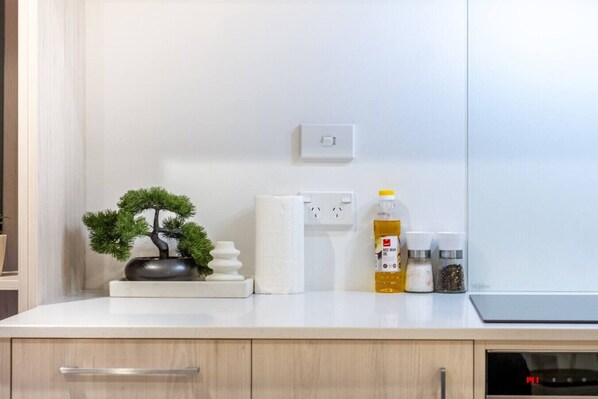 A kitchen counter with a bonsai tree, a bottle of rice bran oil, salt and pepper shakers, and a white towel.