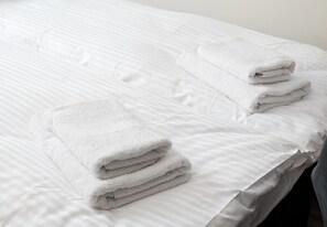 Una cama bien hecha con sábanas blancas y dos toallas dobladas a un lado.
