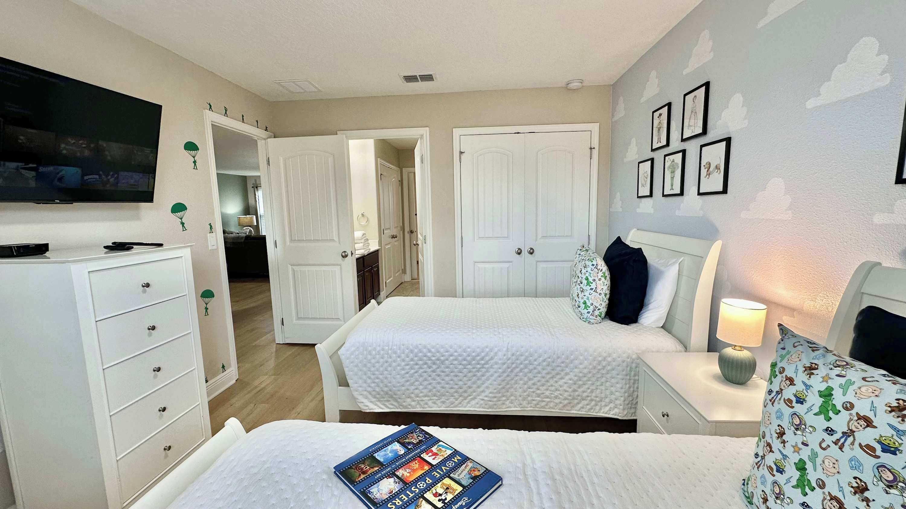A bedroom with two beds, a TV, and a door leading to another room.
