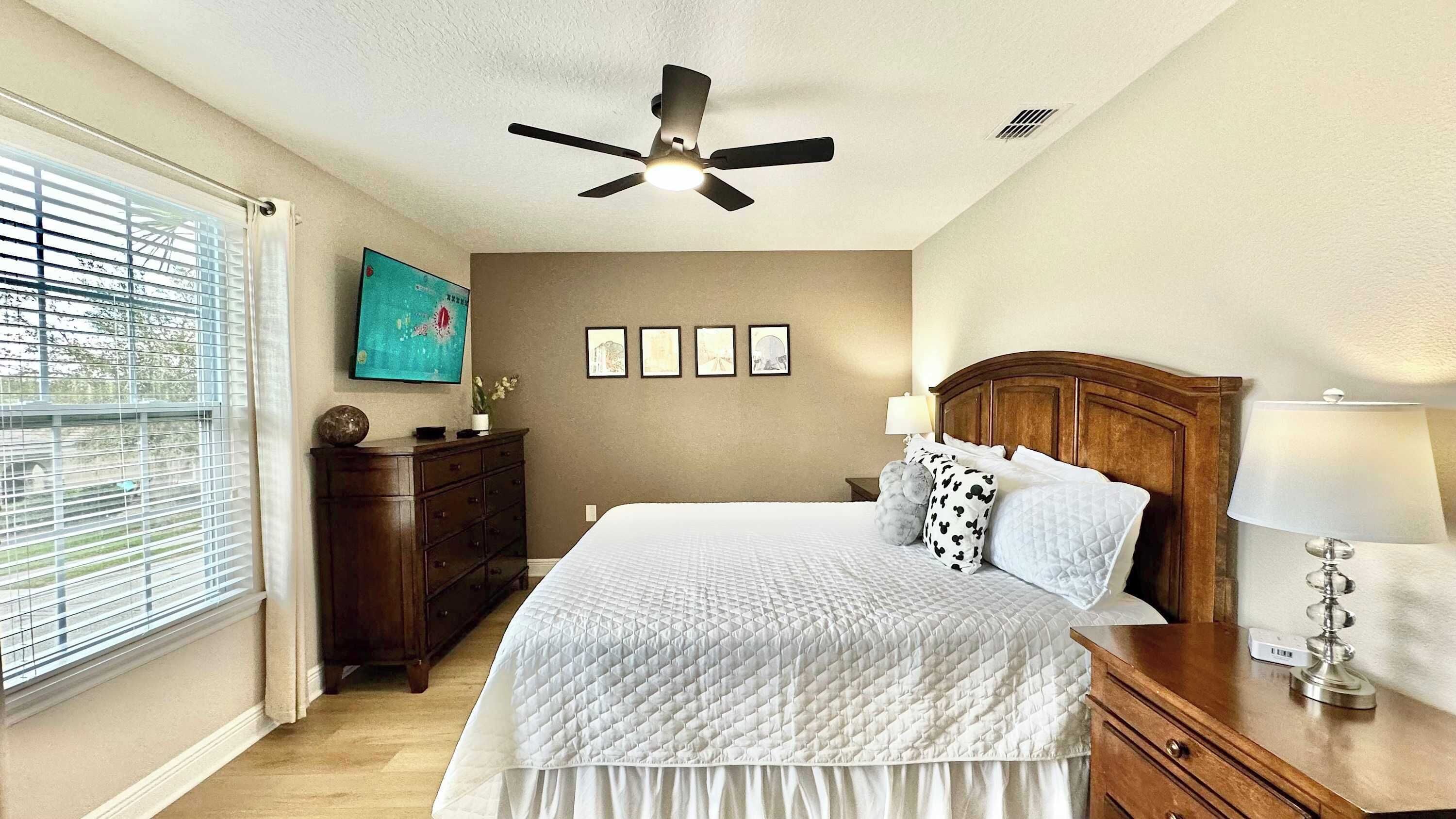 A bedroom with a bed, a nightstand, a dresser, a ceiling fan, and a window with blinds.