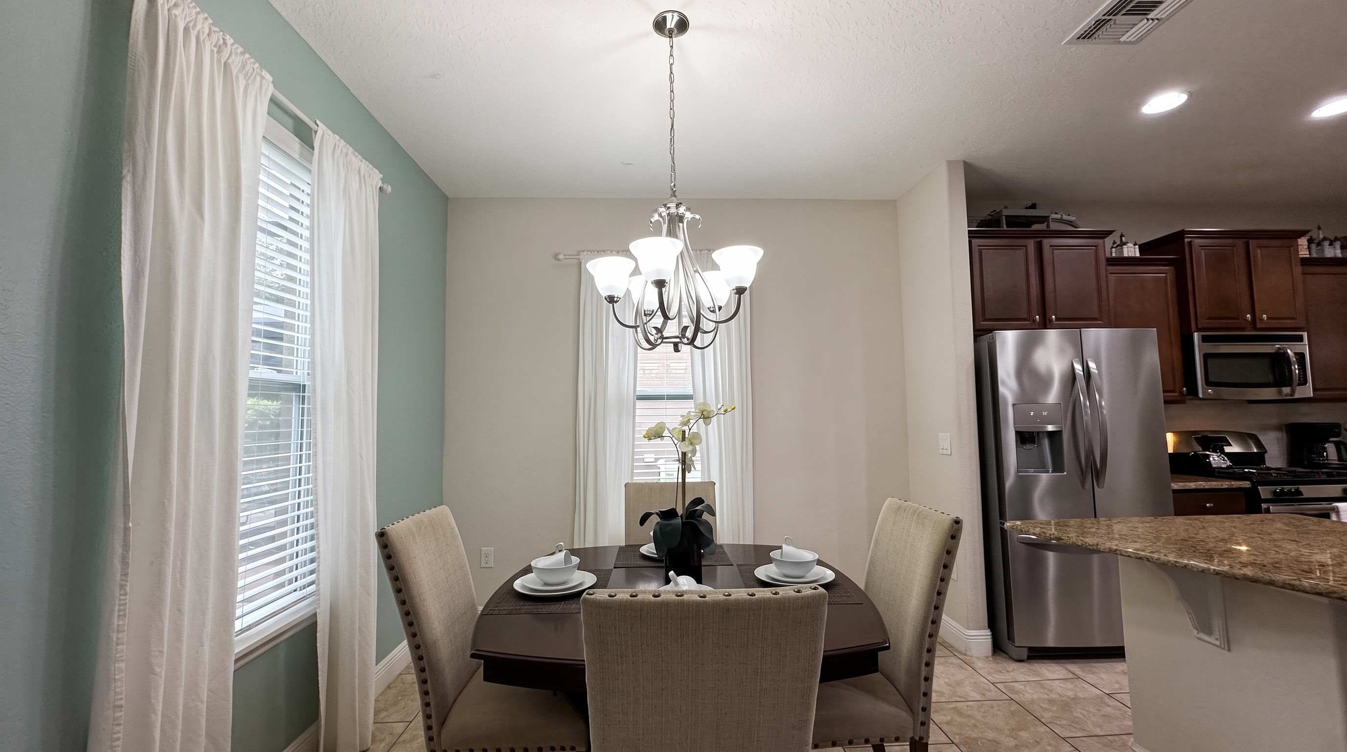 A dining area with a chandelier, a table set for four, and a kitchen with modern appliances.