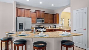 A kitchen with a central island, wooden cabinets, stainless steel appliances, and a white door with a fire safety sign. - The Magic Hideaway at Solterra (Davenport)